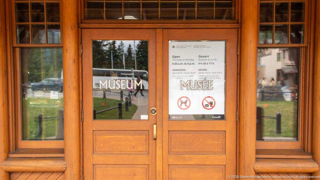 Timber-framed double entrance doors marked MUSEUM and MUSÉE with visitor notices posted on the glass.