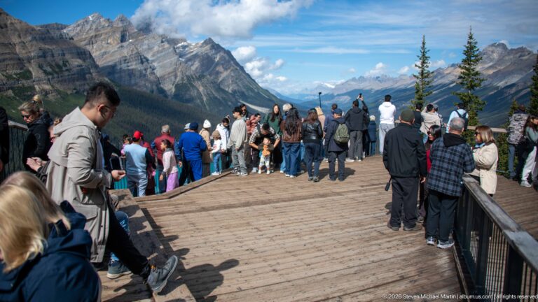 Crowded wooden observation deck at Bow Summit with visitors facing a broad mountain valley and distant peaks.