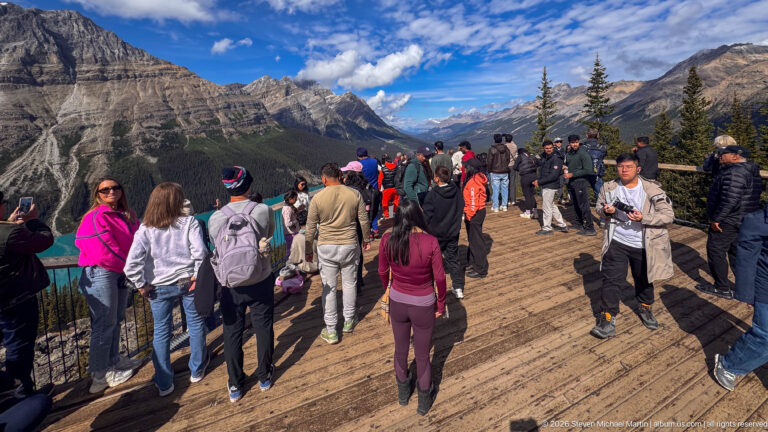 Crowds fill a wooden viewing deck at Bow Summit with layered mountains and a forested valley beyond.