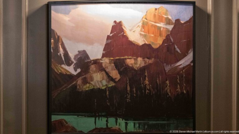 Framed painting of a brightly lit Rocky Mountain peak above dark forest and turquoise water inside the hotel.