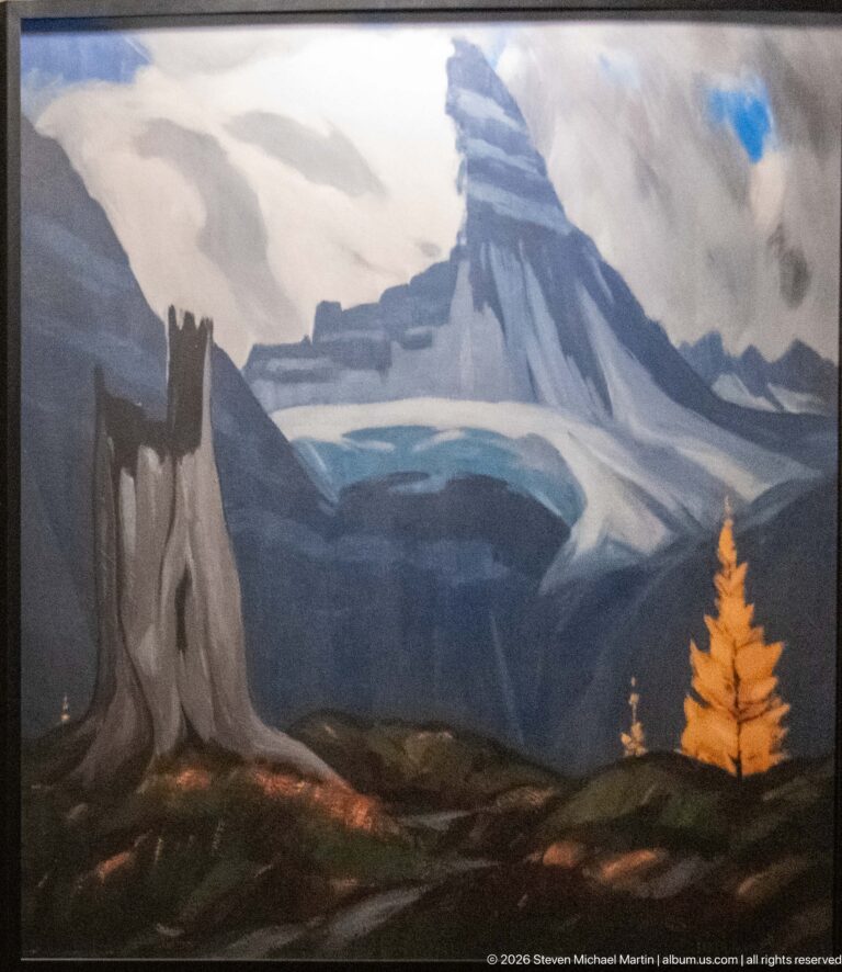 Framed painting of a pointed mountain, pale glacier or snowfield, dark rock formations, blue ridges, and a golden conifer.
