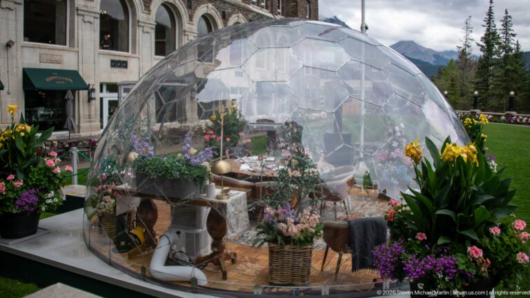 Transparent faceted 360° dining dome furnished with a table and chairs, surrounded by flowers on the Banff Springs Hotel terrace.