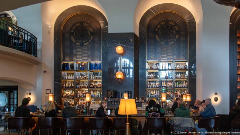 Tall illuminated bottle shelves and dark wall panels behind the busy Rundle Bar, with seated guests and warm pendant lights.