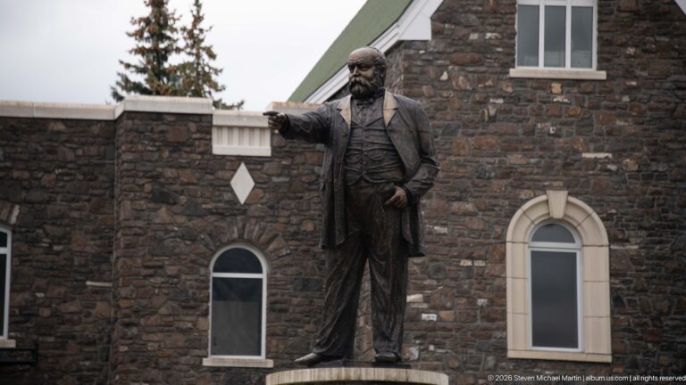 Bronze statue of Sir William Cornelius Van Horne pointing, set against dark stone walls of the Banff Springs Hotel.