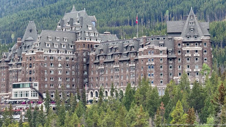 Close exterior view of Banff Springs Hotel with dark masonry walls, rows of windows, dormers, gables, and steep roofs.