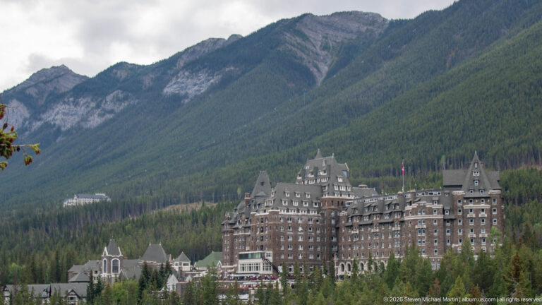 Telephoto view of the Banff Springs Hotel, showing its stone walls, steep roofs, towers, and dormers against a forested mountain.