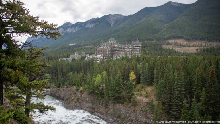 Banff Springs Hotel beyond the fast-flowing Bow River, surrounded by evergreen forest and steep Rocky Mountain slopes.