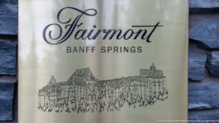 Metal Fairmont Banff Springs sign with cursive logo and line drawing of the hotel mounted against dark stone.