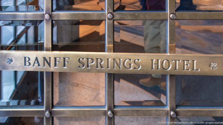 Raised BANFF SPRINGS HOTEL lettering on a metal rail across glass doors with geometric framing and small leaf ornaments.