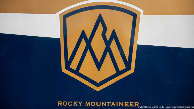 Gold Rocky Mountaineer mountain emblem and lettering on the navy-and-white side of a passenger railcar.