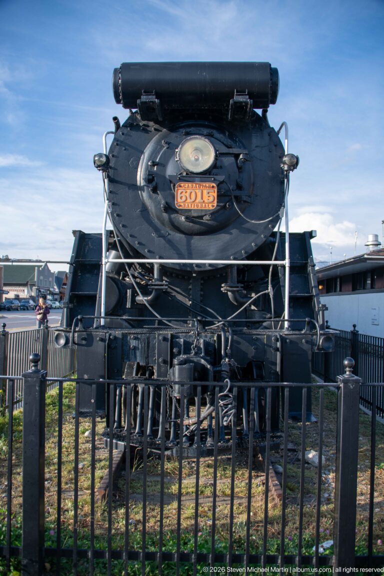 Canadian National steam locomotive 6015 displayed behind a black fence, viewed head-on beneath an open sky.