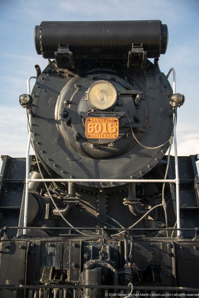 Frontal close view of Canadian National steam locomotive 6015 with smokebox, headlight, handrails, piping, and running gear.