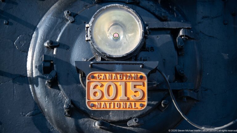 Close view of Canadian National steam locomotive 6015 smokebox, headlight, number plate, bolts, and piping.