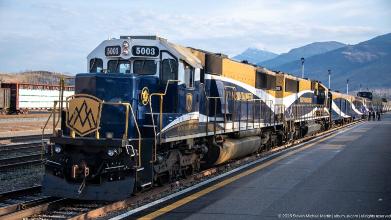 Rocky Mountaineer locomotive 5003 leading a passenger train beside the Banff platform with mountains in the distance.