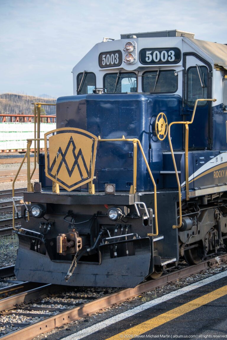 Front and cab of Rocky Mountaineer locomotive 5003 with number boards, yellow rails, coupler, and mountain emblem.