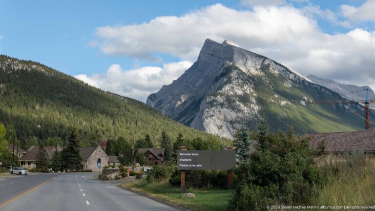 Cascade Mountain rising above a road and low buildings, with pale limestone cliffs and forested lower slopes.