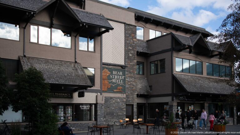 Bear Street Mall exterior with stone piers, dark shingled roofs, storefronts, outdoor tables, and pedestrians.
