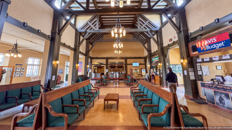 Banff station waiting room with green benches, timber trusses, pendant lights, and an Avis Budget counter at right.
