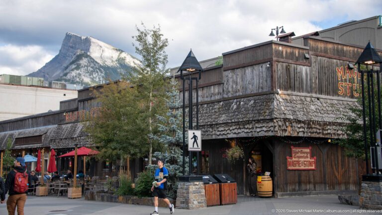 Weathered wood exterior of Wild Bill’s Legendary Saloon beside outdoor dining, with a steep mountain behind.