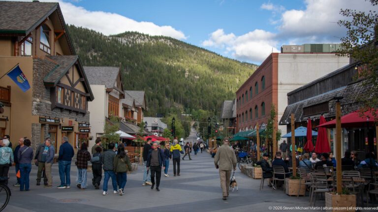 Crowded pedestrian lane between Banff shops and restaurant patios, ending at a forested mountain slope.