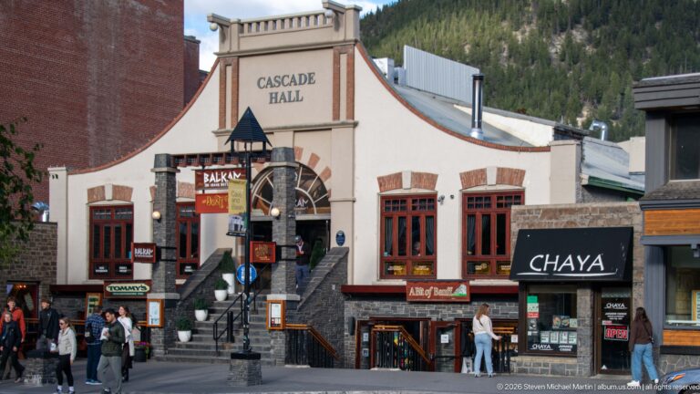 Cascade Hall façade with curved parapet, arched central window, entrance stairs, and ground-floor businesses.
