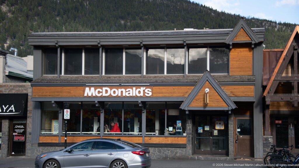 McDonald’s storefront with wood siding, stone base, gabled entrance, and parked car on a Banff street.