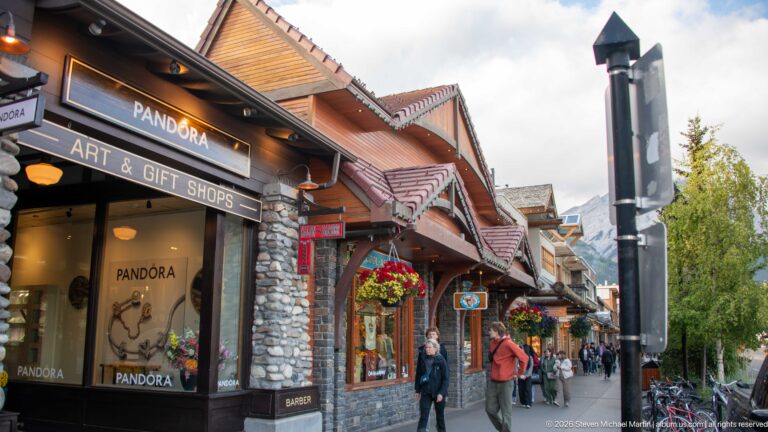 Pandora shop and neighboring stone-and-timber storefronts along a pedestrian-filled Banff sidewalk.
