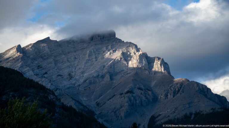 Layered limestone face of Cascade Mountain rising above dark forest beneath low gray clouds.