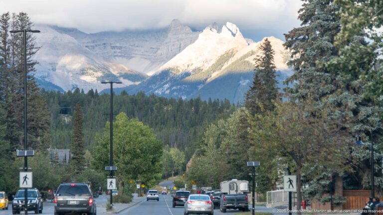 Banff street with cars and pedestrian crossings leading toward cloud-wrapped Cascade Mountain.