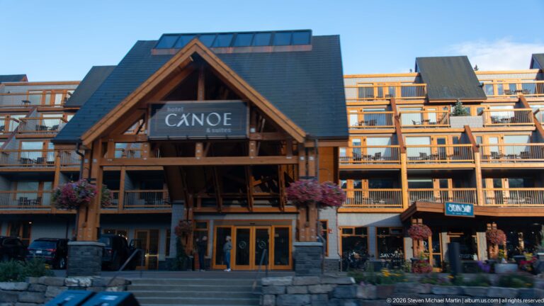 Hotel Canoe & Suites façade with timber entrance gable, stone base, balconies, flower baskets, and dark roofs.