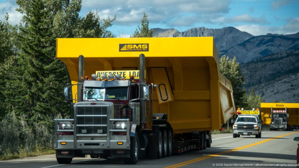 Heavy-haul truck carries a huge yellow industrial module along a mountain highway with convoy vehicles behind.