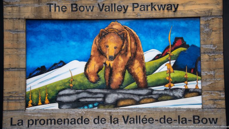 Painted bear and mountain scene on a bilingual sign for the Bow Valley Parkway.