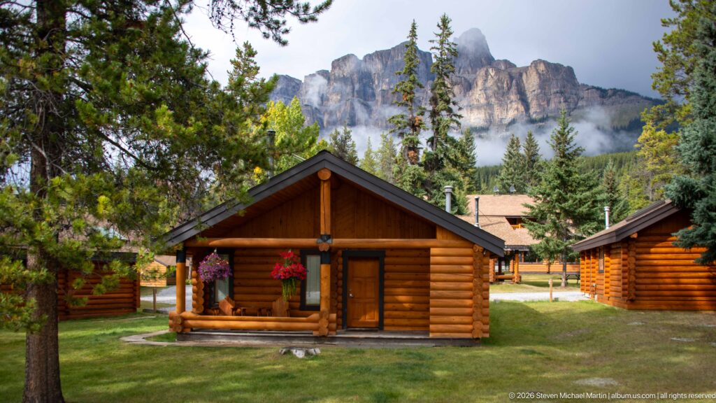 Log cabins and conifers stand below a cloud-wrapped, castellated limestone mountain ridge.