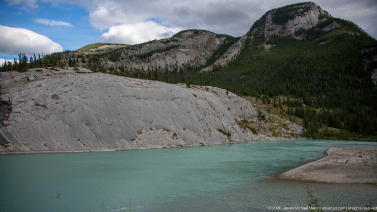 Turquoise river flows beside smooth pale limestone slabs and forested rounded hills.