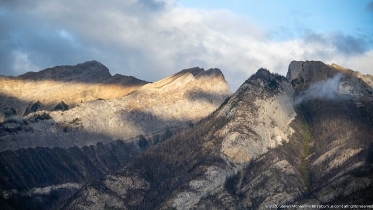 Sunlight crossing pale folded mountain ridges beneath low clouds.