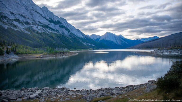 Calm blue-green mountain water reflecting clouds between steep forested slopes.
