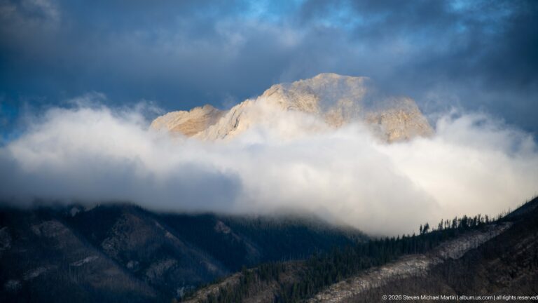 Sunlit pale mountain summit rising above a thick white cloud bank.