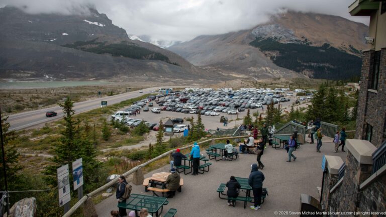 Elevated view over visitor terraces, large parking lot, road corridor, valley floor, and surrounding mountains.