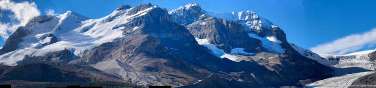 Close telephoto view of jagged mountain cliffs with pale rock bands, snow patches, and small areas of ice.
