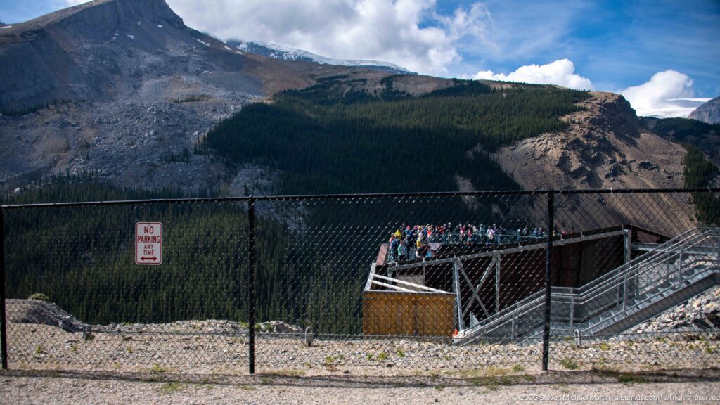 A fenced approach and projecting glass observation platform occupy a steep mountain valley.
