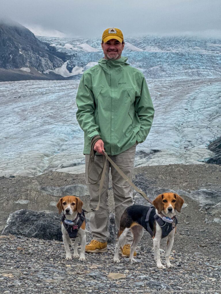 An adult and two beagles fill the foreground while blue-gray glacier ice and debris bands extend across the background.