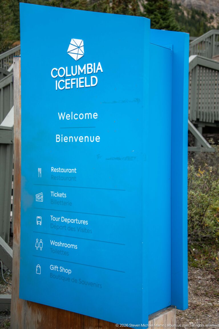 Blue Columbia Icefield Welcome and Bienvenue sign listing restaurant, tickets, tour departures, washrooms, and gift shop.
