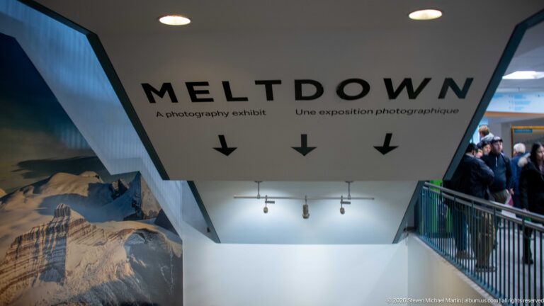 Interior sign reading MELTDOWN, A photography exhibit, with three downward arrows above the gallery entrance.