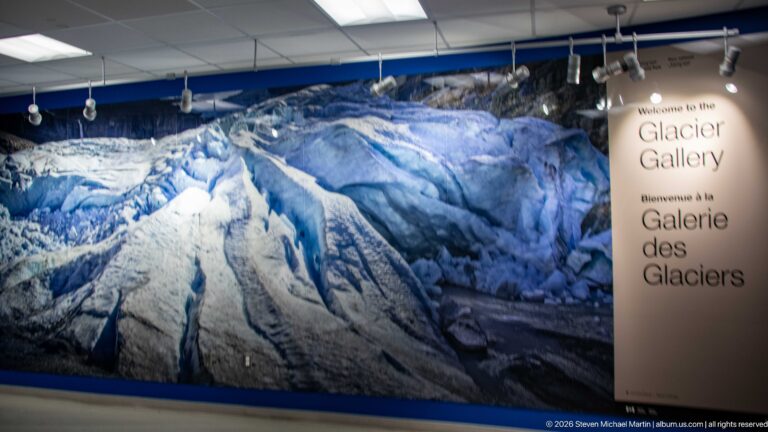 Large panoramic photograph of crevassed glacier ice beside a bilingual Welcome to the Glacier Gallery sign.