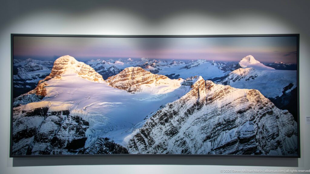 Large panoramic gallery photograph of sunlit snow-covered peaks and a broad high icefield beneath a pastel sky.