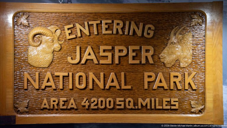 Carved wooden Entering Jasper National Park sign with bighorn sheep and mountain goat reliefs and Area 4200 Sq. Miles text.