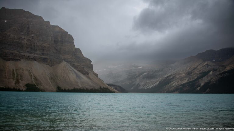 Turquoise lake extends between steep mountain walls beneath dark clouds, with a pale high basin partly obscured in the distance.