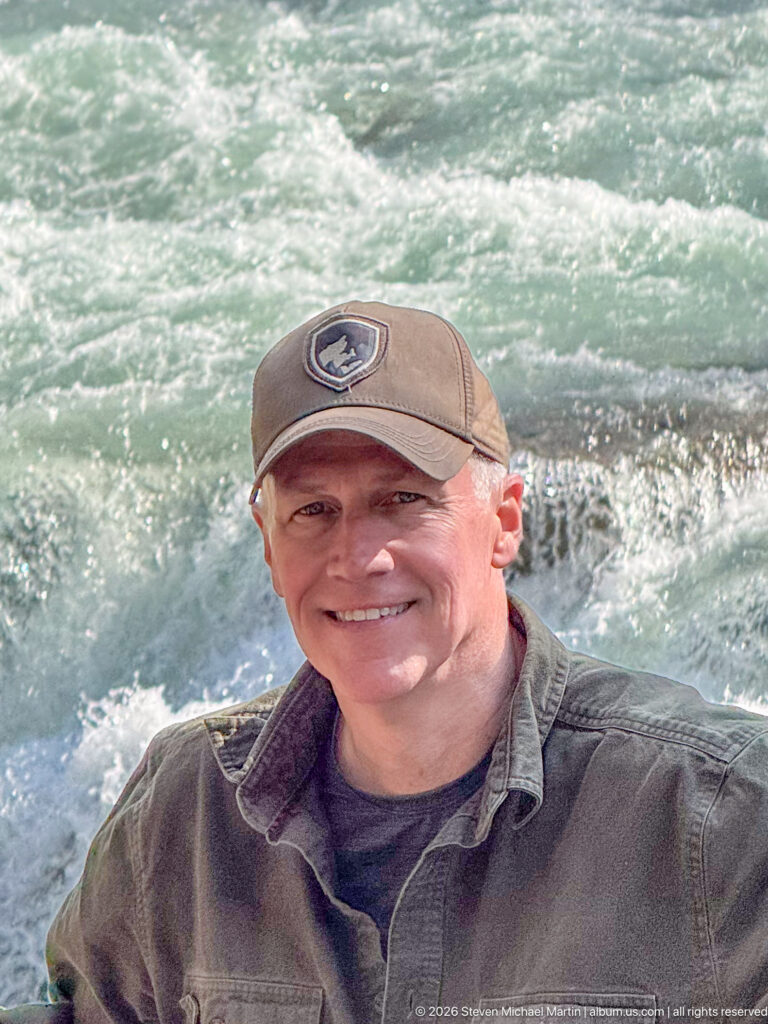 Close portrait of a smiling visitor with foaming turquoise river water directly behind him.