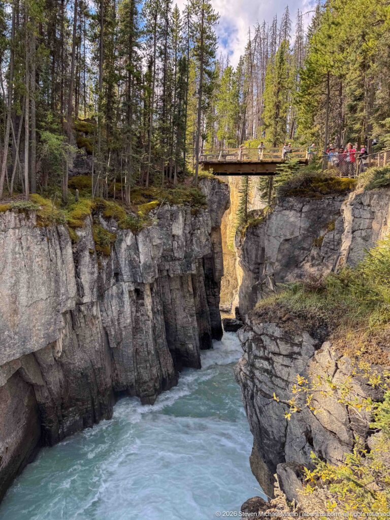 Wooden pedestrian bridge spanning steep rock walls above the narrow Sunwapta River gorge.