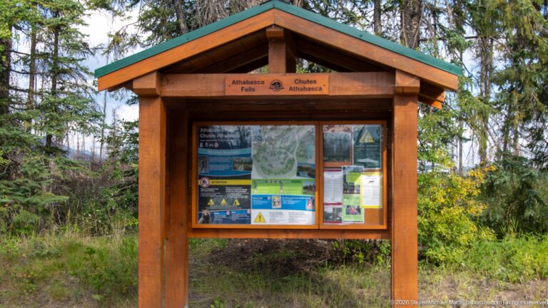 Wooden gabled information kiosk labeled Athabasca Falls and Chutes Athabasca, with maps and notices under glass.